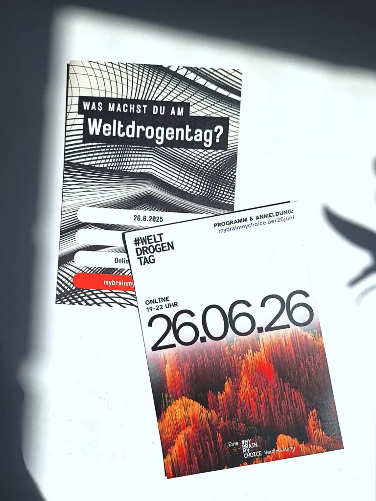 Abbildung der beiden A6 Flyer, der 2025 und 2026 zum Weltdrogentag am 26. Juni einluden bzw. einladen. Motiv 2025: Durch Strich skizzierter vielfältig verzerrter Raum, Motiv 2026: Eine Raumverzerrung in verschiedenen rot-orangen Farbtönen